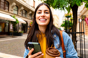 Chica con celular en una mano y un café en la otra, comenzando su día